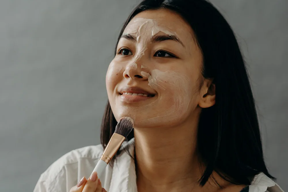mujer aplicando mascarilla facial con una brocha de maquillaje
