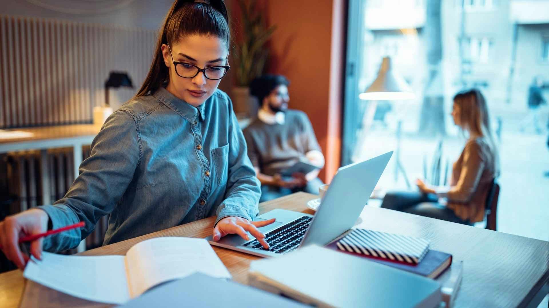 mujer escribiendo en cuaderno frente a laptop