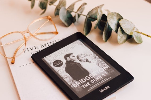 Kindle sobre un libro abierto, al lado de anteojos y planta