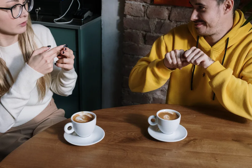 dos personas practicando lenguaje de signos en una cafetería