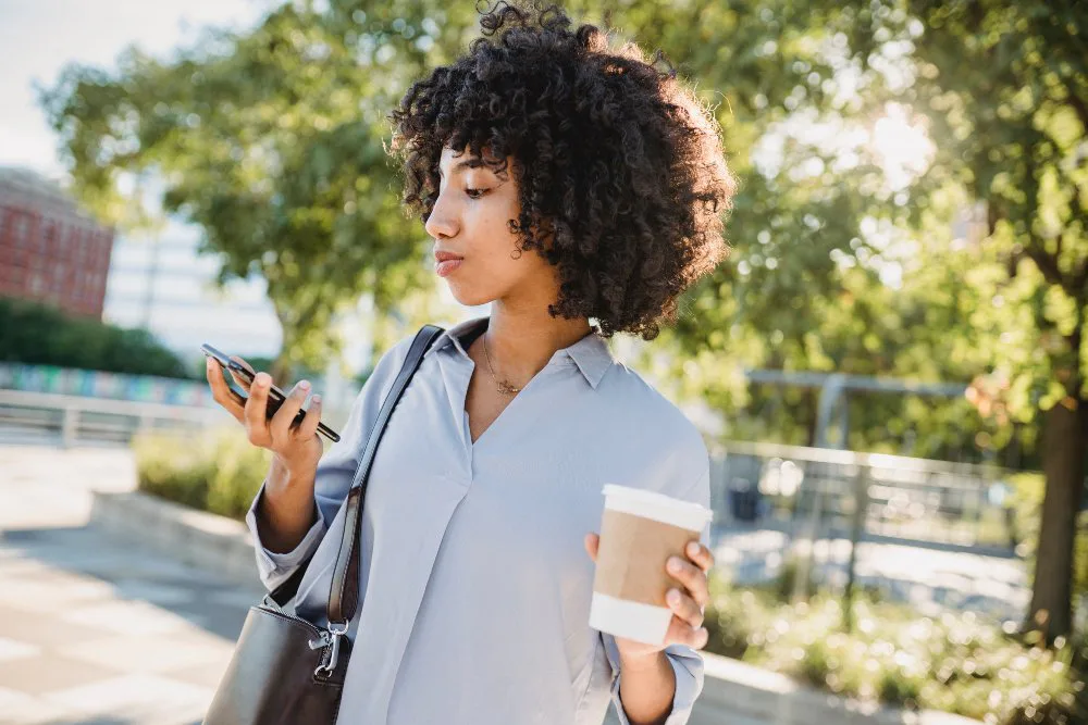 mujer afro con café en una mano y celular en otra mano