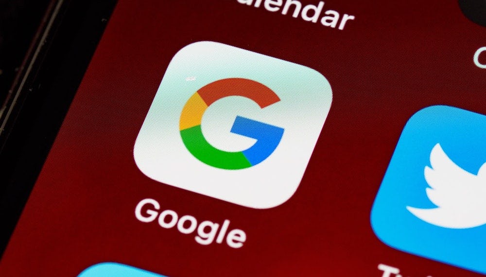 Ícone do aplicativo do Google visto na tela de um dispositivo ao lado do ícone de outros aplicativos sobre um fundo de cor bordô